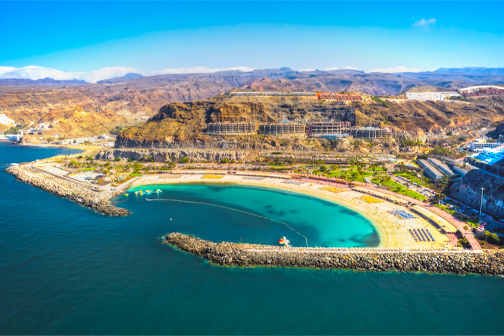 Playa de Amadores op Gran Canaria met een breed zandstrand, helder turquoise water en rotsachtige heuvels rondom de beschutte baai.